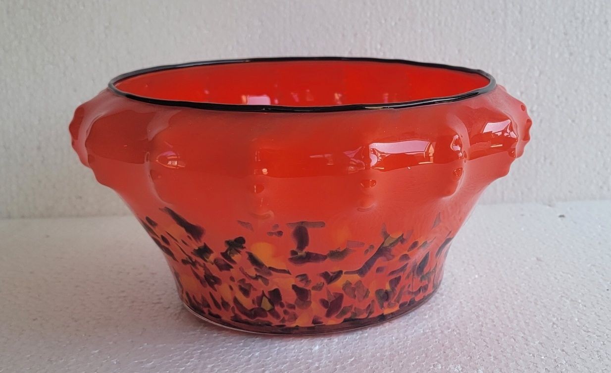 Orange glass bowl with textured sides and black accents, placed against a neutral background.